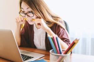 woman biting pencil while sitting on chair in front of computer during daytime . how to focus with adhd