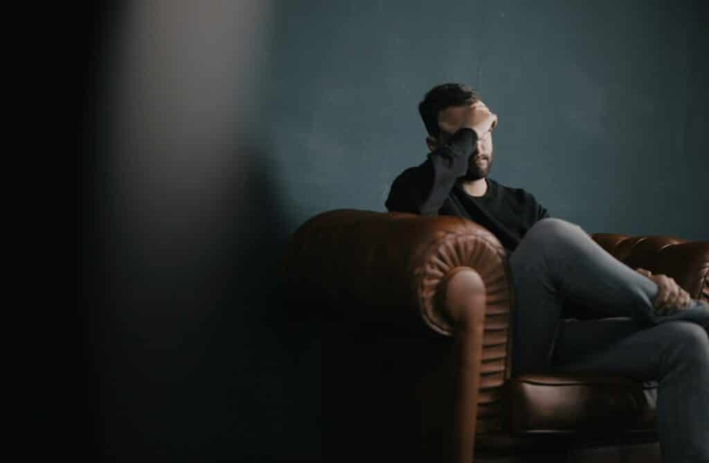 a man holds his head while sitting on a sofa. 7 Types of ADHD